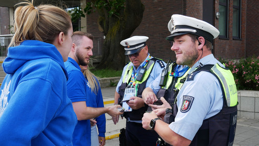 Reportage Einsatzversorgung - Bildergalerie Foto zum Thema "Polizei Einsatzversorgung": Zu sehen ist Svenja, wie sie Patches an eine Gruppe Polizist*innen verteilt.