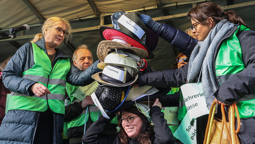 Einer Frau werden mehrere Hüte aufgesetzt, auf denen verschiedene Aufgaben stehen