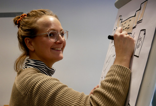 Akademie für Ehrenamtlichkeit Deutschland - ein Seminarbesuch (Bilderstrecke) Zu sehen ist die Nahaufnahme einer Seminarteilnehmerin, die in die Kamera lächelt. In der Hand hält sie einen Edding, mit dem sie ihr Flipchart gestaltet.