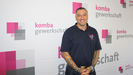 Feuer im Wald - Valentino Tagliafierro Foto zum Thema "Feuer im Wald": Zu sehen ist Valentino Tagliafierro. Er steht vor einer Leinwand mit dem Schriftzug und Logo der komba gewerkschaft.