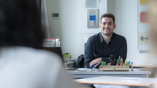 Lehrkräftebildung - Junger BLLV Symbolfoto zum Thema "Lehrkräftebildung": Zu sehen ist ein junger Lehrer, der am Pult sitzt.