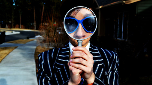 Foto zum Thema "Codes im Arbeitszeugnis": Zu sehen ist eine Frau im Anzug, die durch eine Lupe schaut.