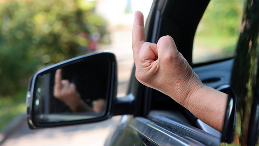 Im Dienst beleidigt - was tun? Foto zum Thema "im Dienst beleidigt": Zu sehen ist jemand, der aus einem geöffneten Autofenster den Stinkefinger zeigt.
