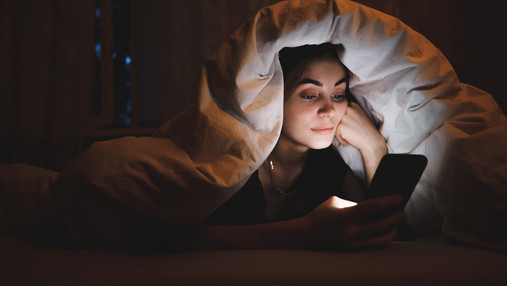 Mediensucht bei Jugendlichen - wenn Smartphone, Computerspiele und Internet zur Sucht werden Foto zum Thema Mediensucht bei Jugendlichen: Eine junge Frau liest im Bett Nachtrichten auf dem Smartphone.