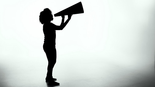 „Kürzt uns nicht weg!“ – Junger DBSH verurteilt Sparpläne Foto zum Thema "Kürzungen Soziale Arbeit": Zu sehen sind die schattigen Umrisse einer Person mit einem Megafon in der Hand.
